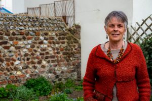 Sue, a white woman with short grey hair, standing in her garden