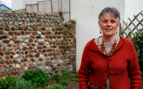 Sue, a white woman with short grey hair, standing in her garden