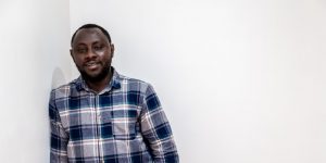 Luqman, a black man in his thirties, leaning on a white wall