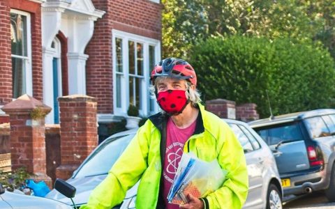 Jim, a white man with grey hair, wearing a face mask and sitting on a bicycle