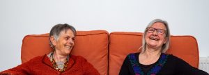 Sue and Annie, two white women, sitting together on a sofa and smiling