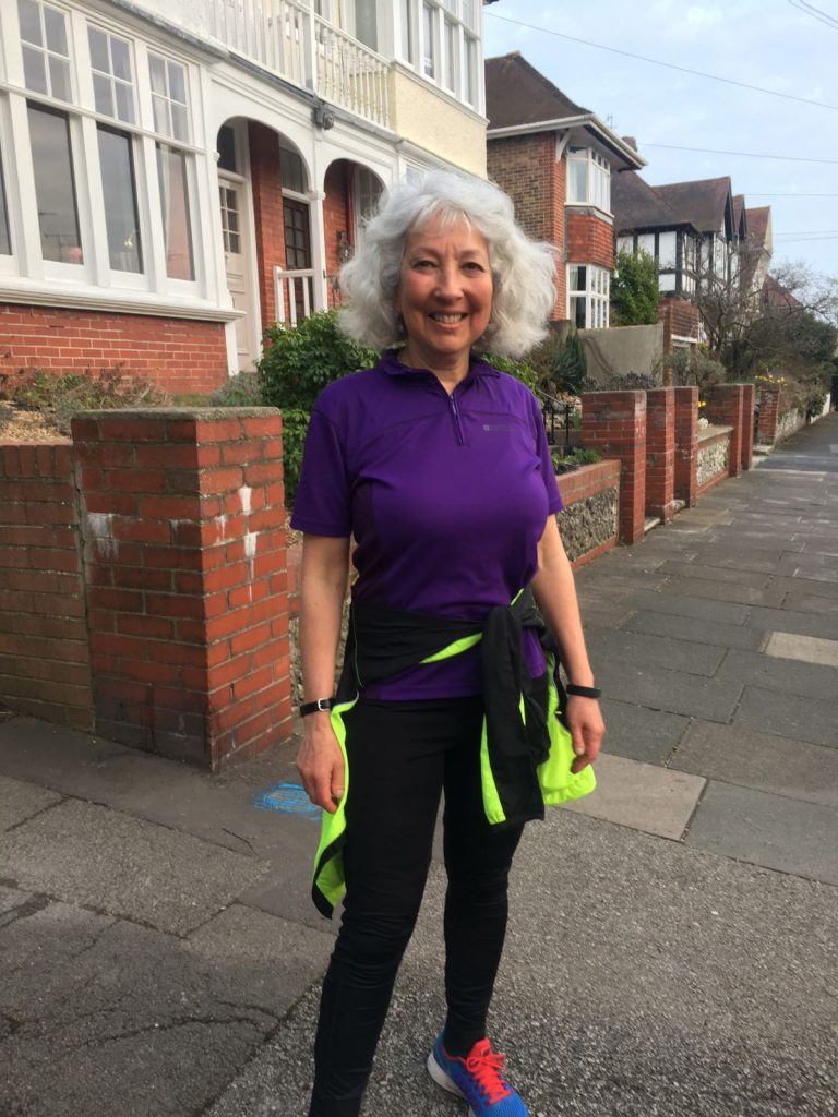 Karen, a woman in her 60s, stands in her purple and black running gear on a residential street