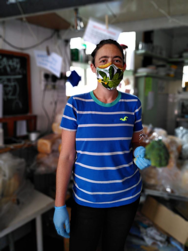 A white woman in her thirties holds a brocolli and wears one or our masks. The mask has a leaf pattern design