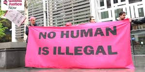 People on a protest, holding a banner which reads 'No Human is Illegal'